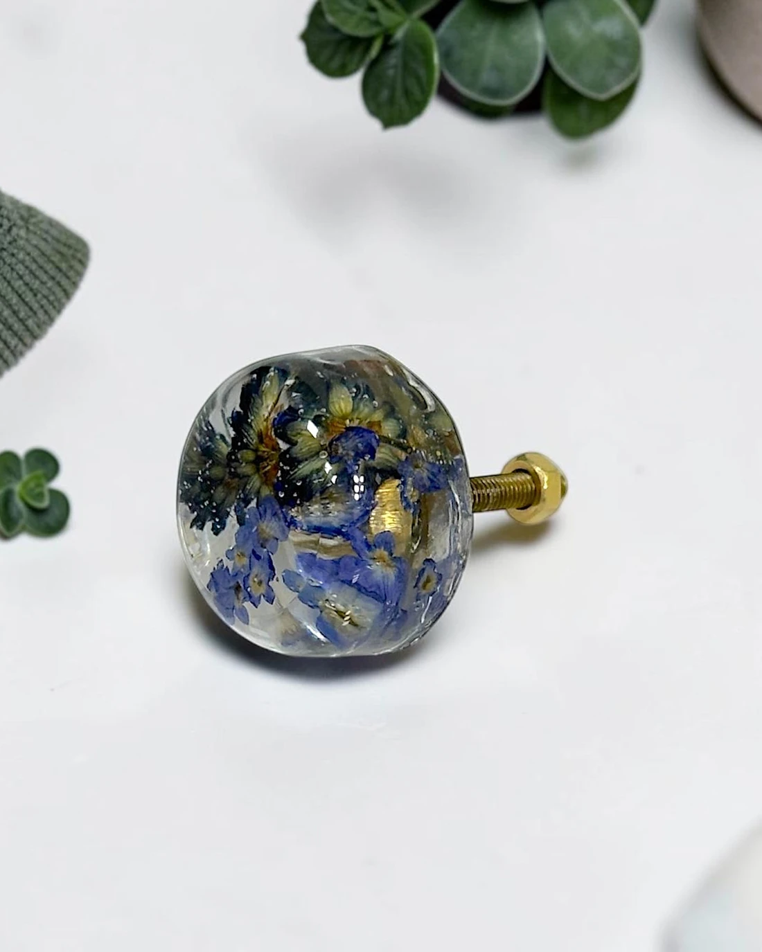 Gałka meblowa Lawenda (Lavandula officinalis) · gałka ze śrubą na białym blacie, wokół zielone listki